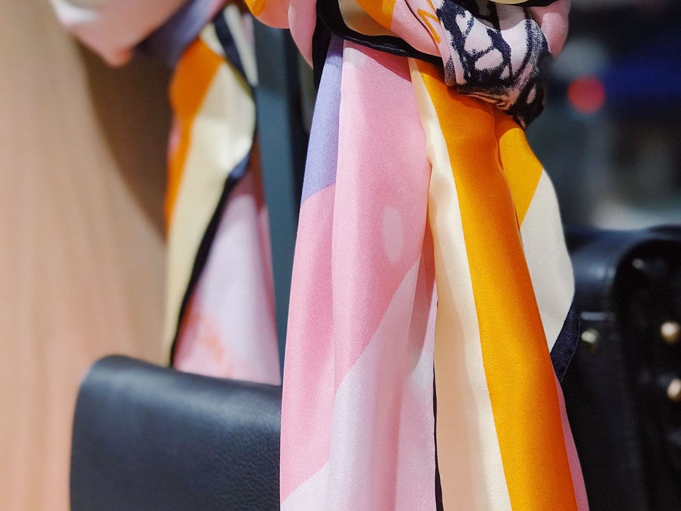 Foulard en soie rose, orange et violet noué à un sac à main noir